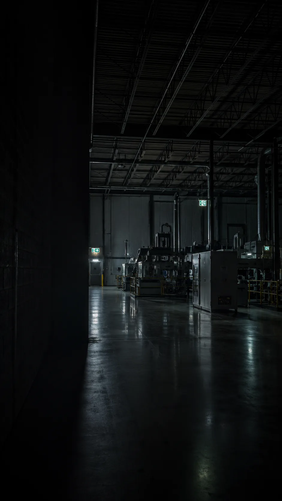 A plant floor at a standstill, lit only by exit and emergency lighting, machines idle.